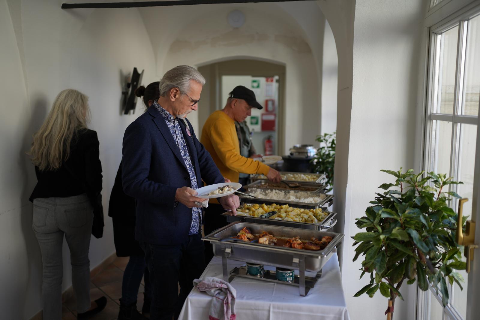 In einem Durchgang ist das Buffet-Essen aufgestellt, Teilnehmer des Kongresses nehmen sich von dem Essen, Mann ist im Vordergrund zu sehen