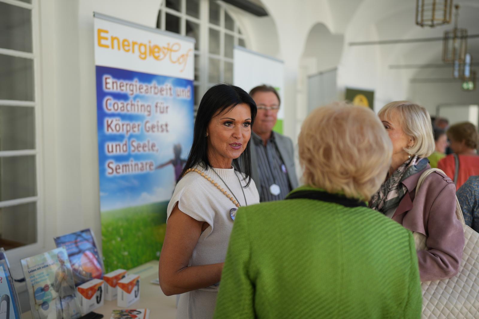 Vor einem Stand mit der Schrift ,,Energiehof" stehen zwei Damen die miteinander auf dem Kongress sprechen