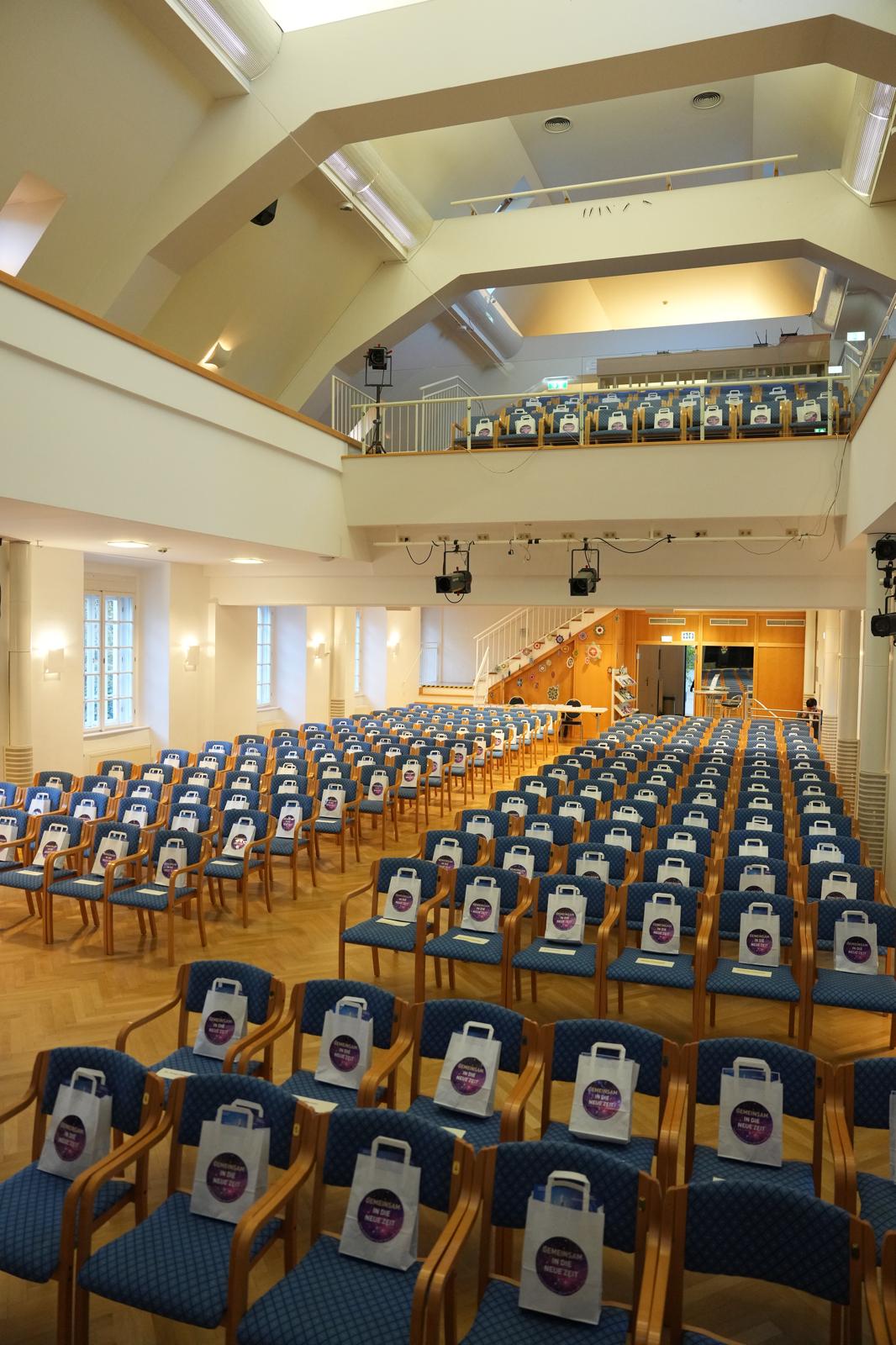 Ein leerer Saal mit einigen Sesselreihen. Auf den Sesseln sind vorbereitete Taschen für die Teilnehmenden des Kongresses