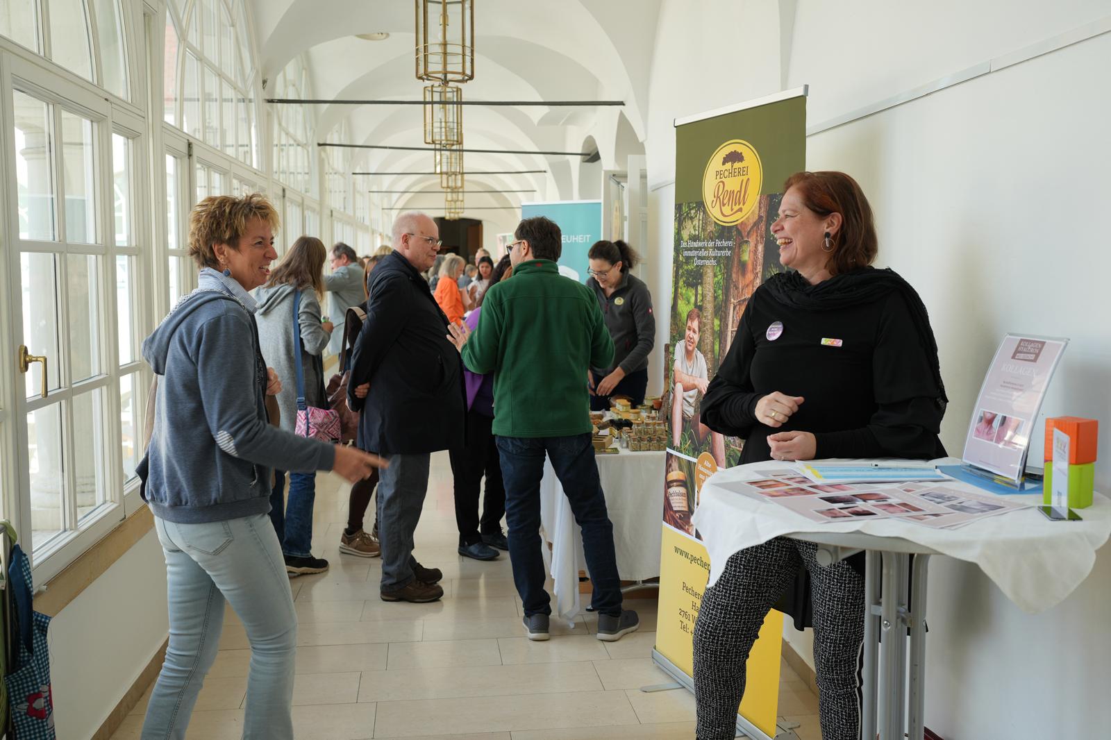 Ein Gang mit mehreren kleinen Ständen unterschiedlicher Themen, Menschen die miteinander reden