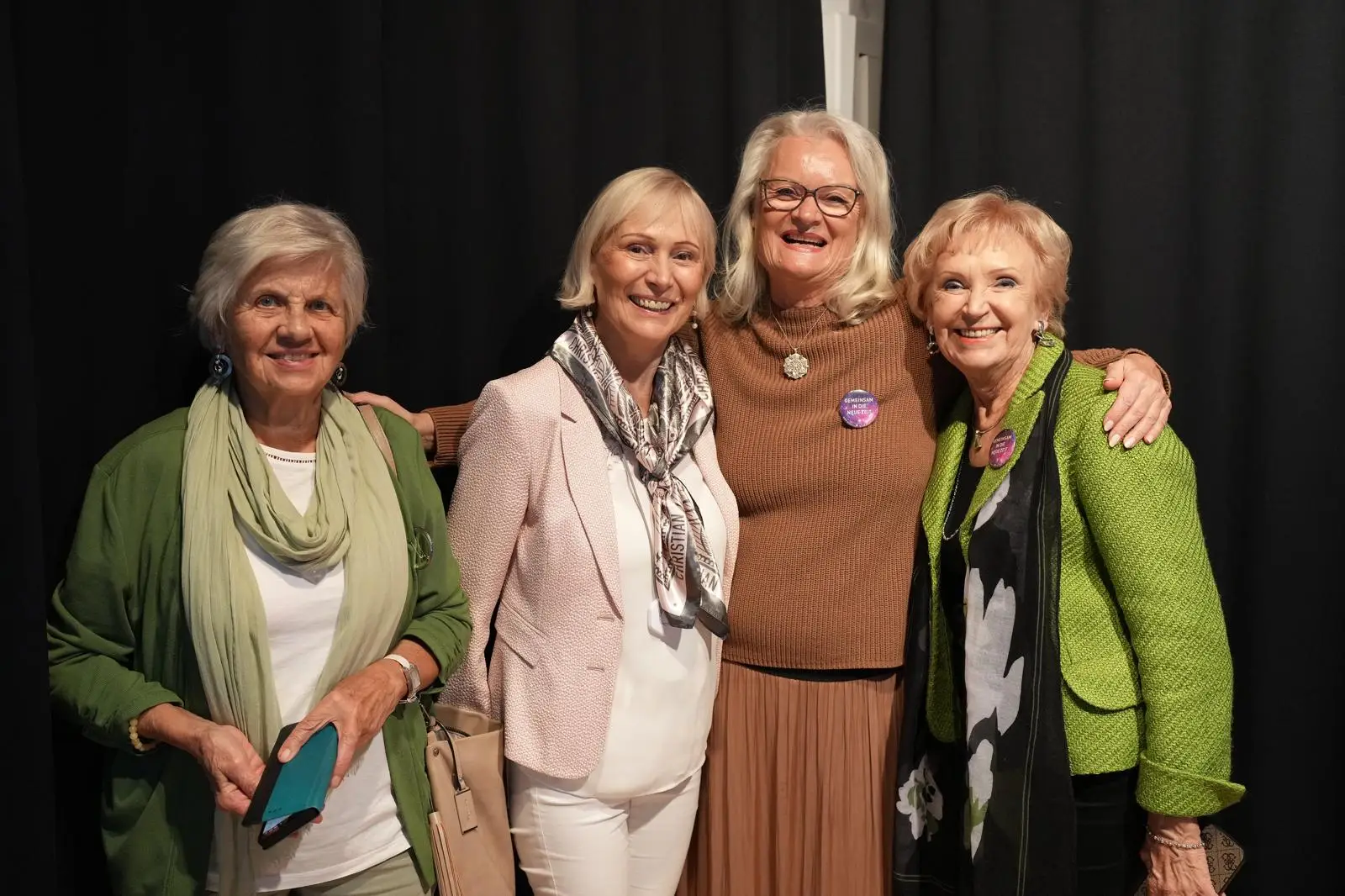 Vortragende steht mit mehreren Frauen in einer Gruppe und lächeln in die Kamera vor einem dunklen Hintergrund