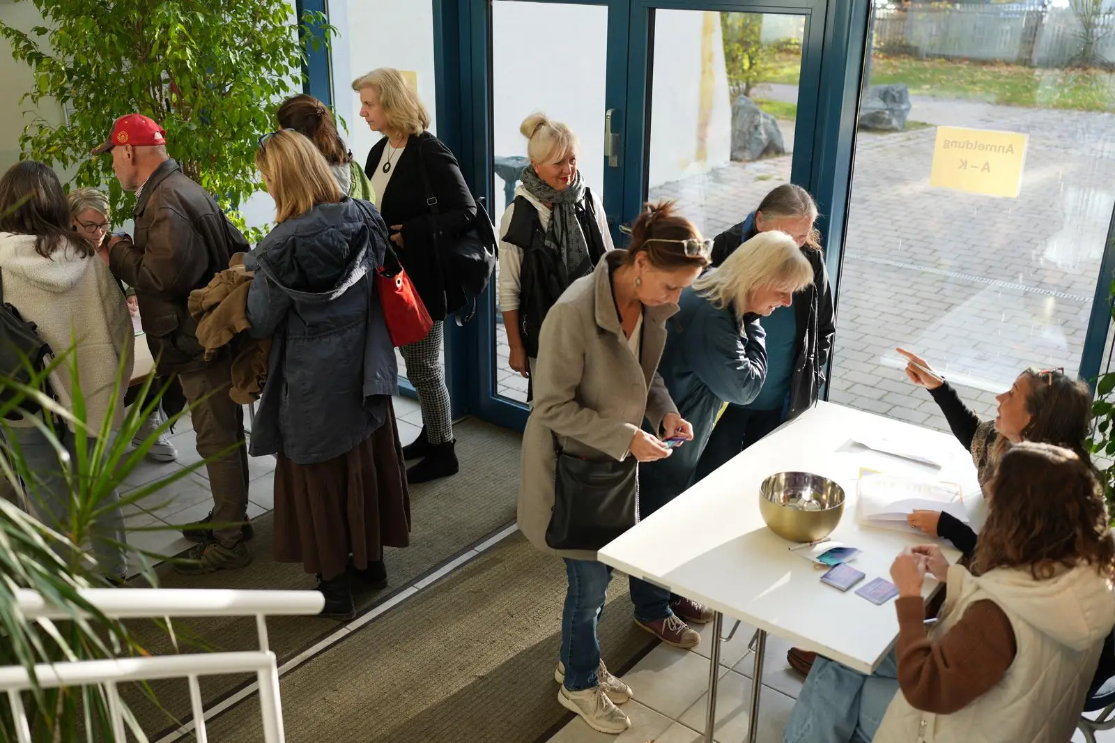 eine Gruppe an Menschen steht bei einem Tisch und eine andere Gruppe wartet auf den Einlass.